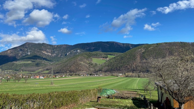 View from the terrace, © Wiener Alpen View from a terrace of green fields and wooded hills under a blue sky with clouds.