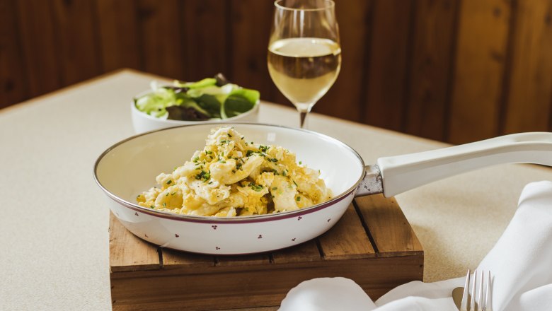 Popular classic: egg dumplings, © Niederösterreich Werbung/David Schreiber Egg dumplings in a pan with a glass of white wine and a salad in the background.