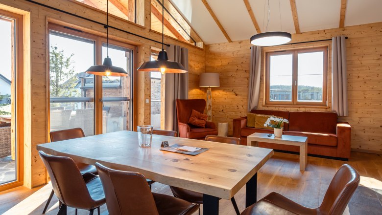 Kittenberger Chalets at the Gartensee, © Niederösterreich Werbung / Maximilian Pawlikowsky Interior view of a modern chalet with wooden walls, dining table and chairs, large windows and cozy seating area.