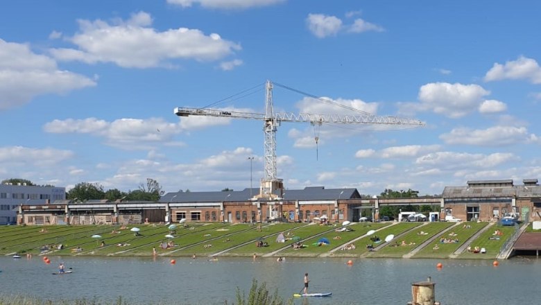 korneuburg-danube-werftbad-liegewiese, © SEFKO People relaxing on a lawn by a river with a crane in the background.