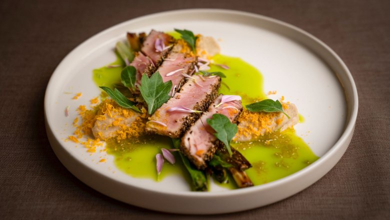 Fine dishes at the Sporthotel, © Sporthotel Semmering An artfully prepared dish with meat, green sauce and edible flowers on a white plate.