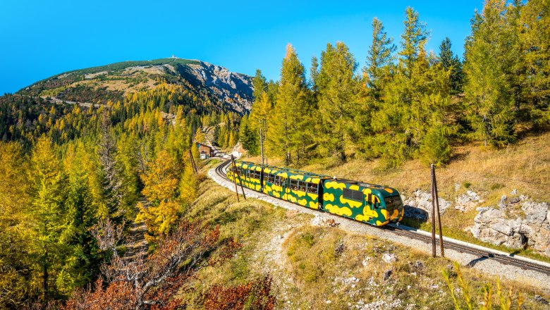 The salamander train passes through the landscape, © NB-Zwickl A train in salamander design travels through an autumnal mountain landscape with a blue sky.