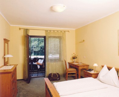 Room view, © z.V.g. von Café Restaurant Bernhart A cozy hotel room with double bed, desk, chest of drawers and balcony with a view of the greenery.