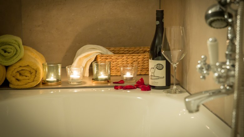 Bathroom romantic suite, © Schlossschenke Romantic bathroom with candles, wine bottle and rose petals on the edge of the bathtub.