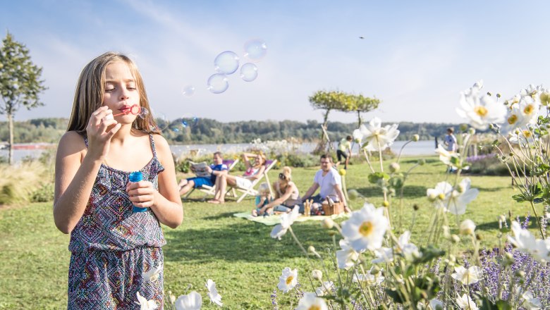 donaulaende_c_robert-herbst-stadtgemeinde-tulln, © Robert Herbst/Stadtgemeinde Tulln Girl making soap bubbles in a park with flowers and people in the background.