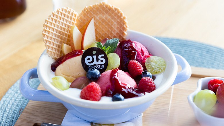 Eis-Greissler coffee house Joghurtweidling, © Blochberger Eisproduktion GmbH Ice cream sundae with yogurt, fruit ice cream, fruit and waffles on a wooden board.