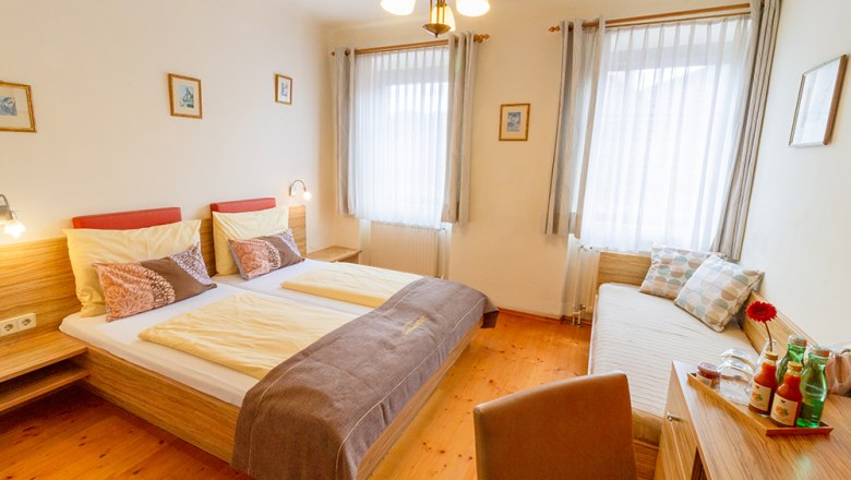 Guest room, © Annemarie Heller A cozy guest room with double bed, day bed, wooden furniture and decorative cushions. Bright curtains and pictures on the walls.