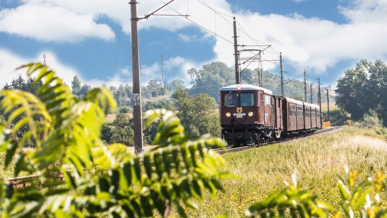 Ötscherbär family adventure train, © NÖVOG/ Roman Gerstl A nostalgic train travels through a green landscape with a blue sky.