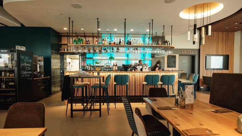 free bar area, © Michael Reidinger Modern bar area with wooden tables and blue bar stools, illuminated by hanging lamps.