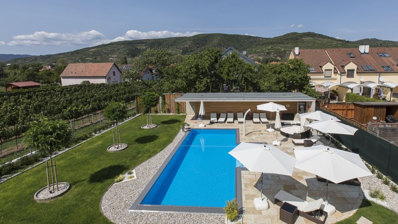 Swimming pool area with sun loungers and parasols, © Weinlodge Siedler A modern pool with sun loungers and parasols in a well-tended garden surrounded by hills and houses.