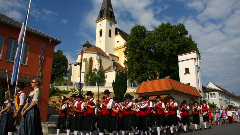 Church, © Gemeinde Auersthal A brass band in traditional dress marches in front of a church.