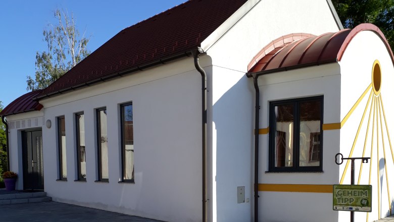 Amethyst Chapel Grübern, © Stadtgemeinde Maissau White chapel with red roof and yellow accents, surrounded by paved floor and plants.
