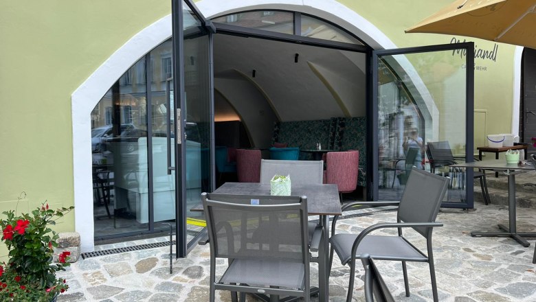 Exterior view of the café, © @JF Exterior view of a café with open glass doors and outdoor seating.