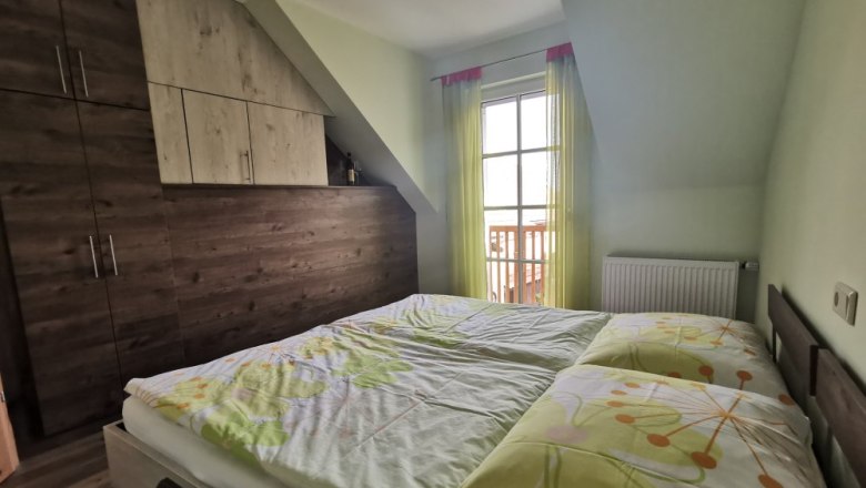 Grüne Veltliner" vacation apartment, © Weinhof Brauner Bedroom with double bed, wooden wardrobe and window with yellow curtains.
