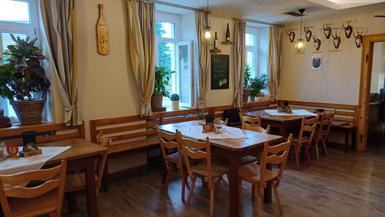 Dorfstub'n Wartmannstetten, © Wiener Alpen Interior view of a cozy dining room with wooden tables and chairs, decorated with plants and deer antlers on the wall.