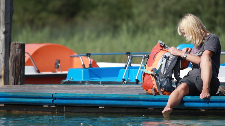 Relaxing at Lake Erlaufsee, © weinfranz.at Person sitting on a jetty on Lake Erlaufsee with their feet in the water, next to a rucksack. Pedal boats can be seen in the background.