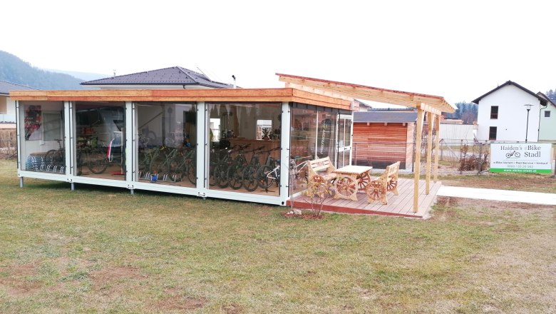 haidens_ebike_stadl-exterior-view-bike-rentalkirchbergathaidens-ebike-stadl, © Haiden´s eBike Stadl Exterior view of a modern bike rental shop with a glass front and wooden roof, surrounded by lawn and a sign reading 'Haiden's eBike Stadl'.