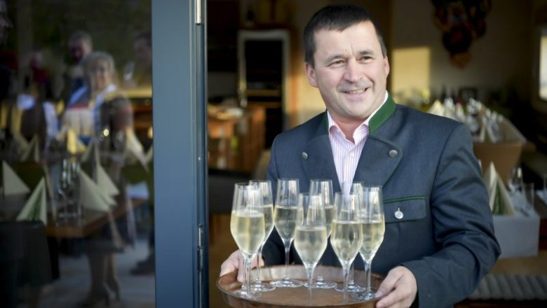 Czipin Leonhard serves, © Robert Herbst A man in traditional dress serves champagne glasses on a tray.