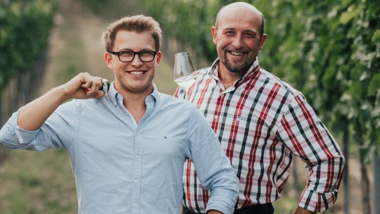Winemaker Paul and his father are a strong team, © Winzerhof Zimmermann Two men stand smiling in a vineyard, one holding a wine glass.