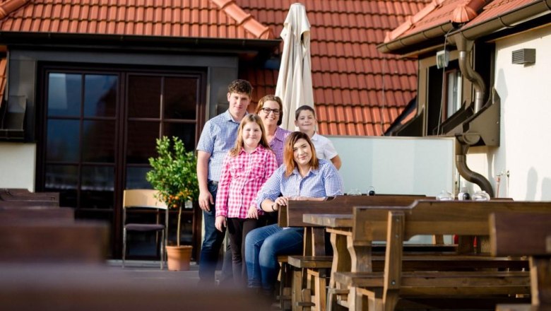 Kropf family, © Alexander Pfeffel A family poses on a terrace with wooden tables and red roof tiles in the background.