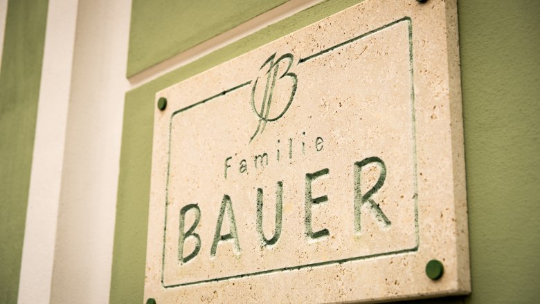 Family Bauer, © © Weingut Josef Bauer Stone plaque with the inscription 'Familie Bauer' on a green wall.