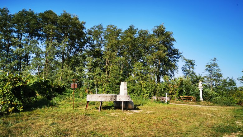 Tranquil vacation cruise, © Weinstraße Weinviertel Meadow with benches and sculptures in front of trees and a blue sky.