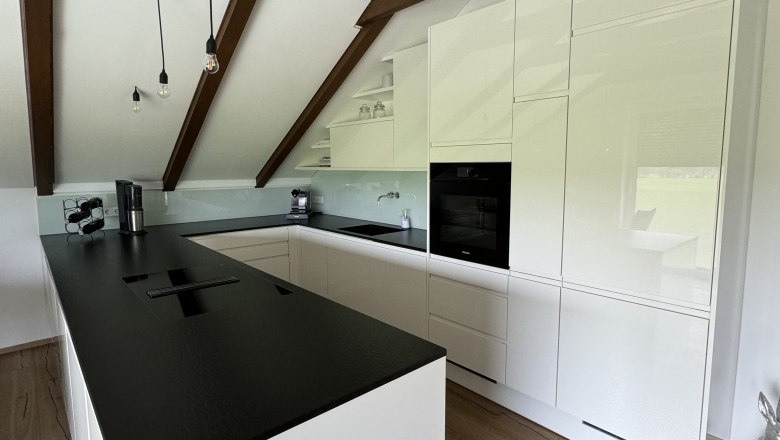 High-quality equipped kitchen, © Juwel am Stadtrand Modern kitchen with white cupboards, black worktop and wooden beams on the ceiling.
