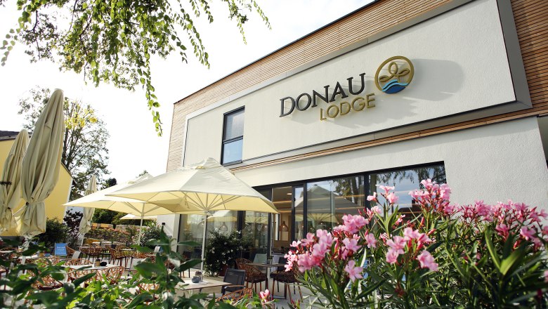 Danube Lodge, © weinfranz Exterior view of the Donaulodge with terrace, parasols and flowering plants.