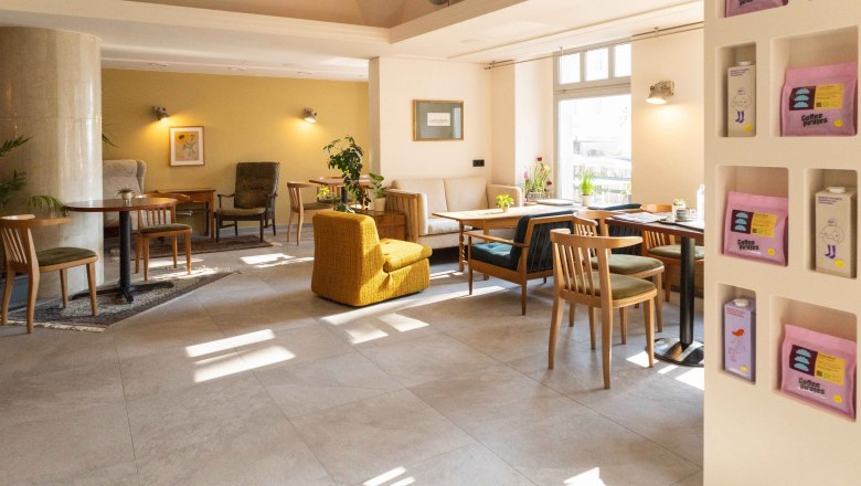 BREADLEY BISTRO, © Marie Grulich Interior view of a cozy café with wooden furniture and plants.