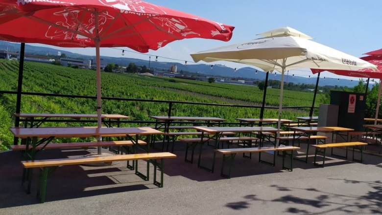 In the Leithen wine cellar lane, © Weinbau Maier Beer garden with tables and parasols in front of a vineyard.
