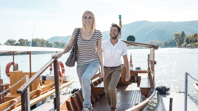 Car-free travel in the Wachau, © Donau Niederösterreich/Steve Haider A man and a woman step off a boat onto a jetty. A river and wooded hills can be seen in the background.