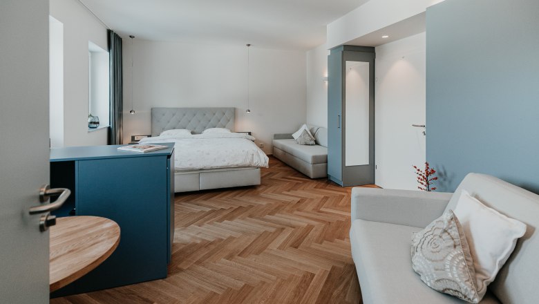 Relax in the new cozy rooms, © Der Löffler - Nicole Seiser Modern furnished hotel room with double bed, sofa and wooden floor.