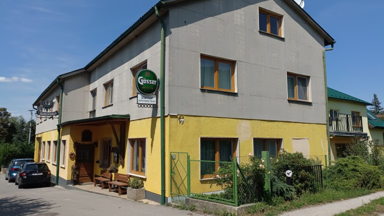 TDR-Gasthof Schwarzer Adler exterior view, © Márton Varga Exterior view of a yellow-grey inn with Gösser sign and parked cars.