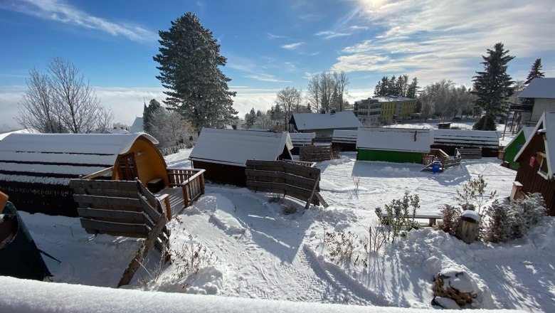 Glamping Park in winter, © Glamping-Park Mönichkirchen OG Winter glamping park with snow-covered huts and trees under blue skies and sunshine.