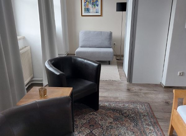 Guest room Weixelbaum, © Familie Weixelbaum Modern guest room with two leather armchairs, carpet, gray armchair and artwork on the wall.