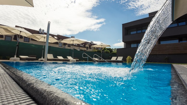 Outdoor pool with waterfall, © KASTNER NEW MEDIA - kastner.tv A modern pool with waterfall, surrounded by sun loungers and parasols, in sunny weather.