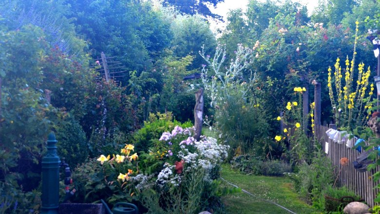 5cf7b1af-5123-422e-be3e-e81130fb86bb_farbe_ausschn, © Familie Mahr A lush garden with various flowers and bushes, a green tap and a watering can in the foreground.