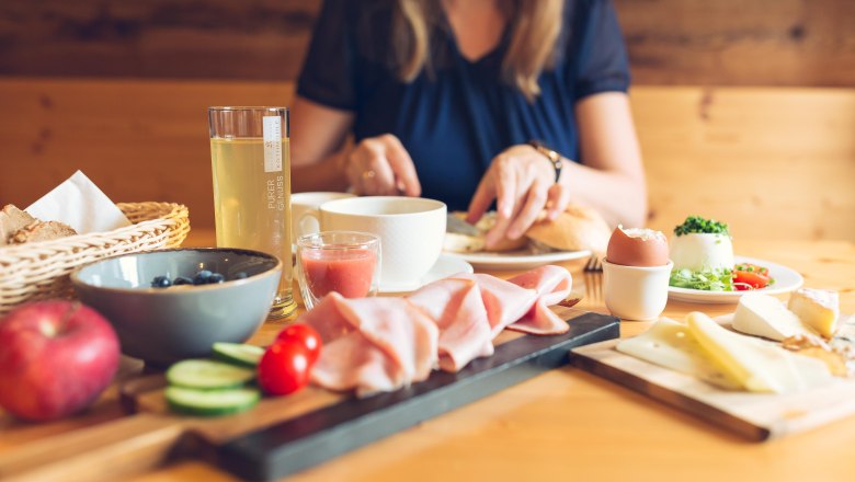 RelaxResort Kothmühle, © Johanna Meinschad Breakfast table with cold cuts, cheese, egg, fruit and drinks, woman in the background.