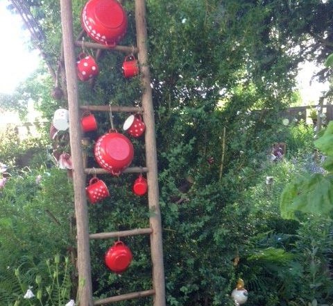 Creative ideas in the garden, © Erika Pascher A wooden ladder in the garden, hung with red pots and cups with white dots.