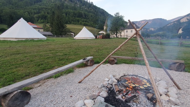 Fireplace - Wilderness Center Nasswald, © Jonathan Clark Campfire with barbecue over a fireplace, tents in the background, surrounded by mountains and meadows.