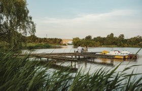 Landscape pond in Bernhardsthal, © Michael Reidinger A couple sits on a jetty by a pond in Bernhardsthal, surrounded by nature and pedal boats.