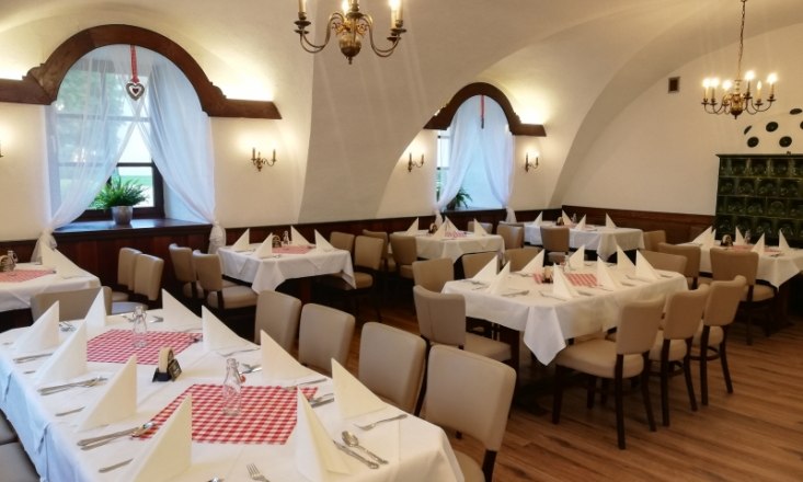 The guest room, © Reichenauer Schloss-Stube Guest room with laid tables, white tablecloths and red napkins, chandeliers and vaulted ceiling.