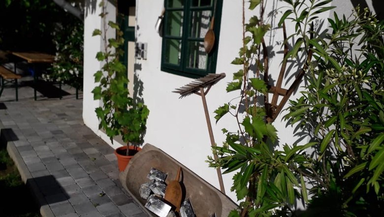 Inner courtyard, © Weingut Wagner White building with green shutters, plants and garden tools on the wall.