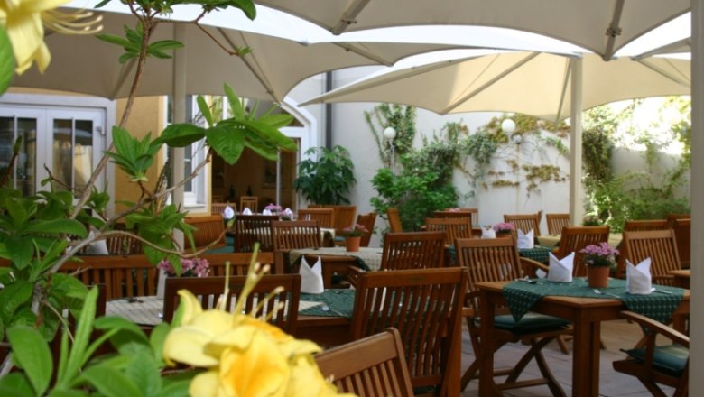 Guest garden at the Hotel-Restaurant Zur Post, © Hotel-Restaurant Zur Post A cozy guest garden with wooden furniture and parasols, surrounded by plants.