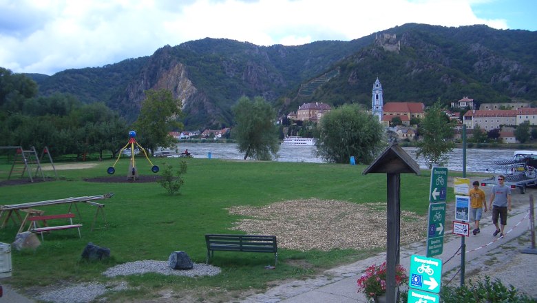 Rossatz bathing area, © Gemeinde Rossatz-Arnsdorf Green meadow with playground, river and mountains in the background.
