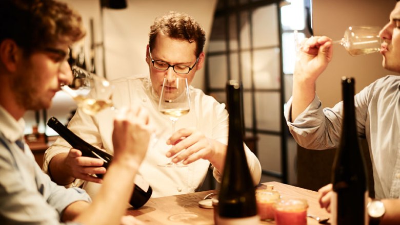 The wine list with 2,500 items also includes the Weinhofmeisterei Mathias Hirtzberger, © Michael Winkelmann Three men tasting wine at a table with bottles of wine.