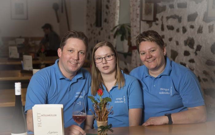 12b4574, © Josef Salomon Three people in blue shirts sit at a table in a rustic room.