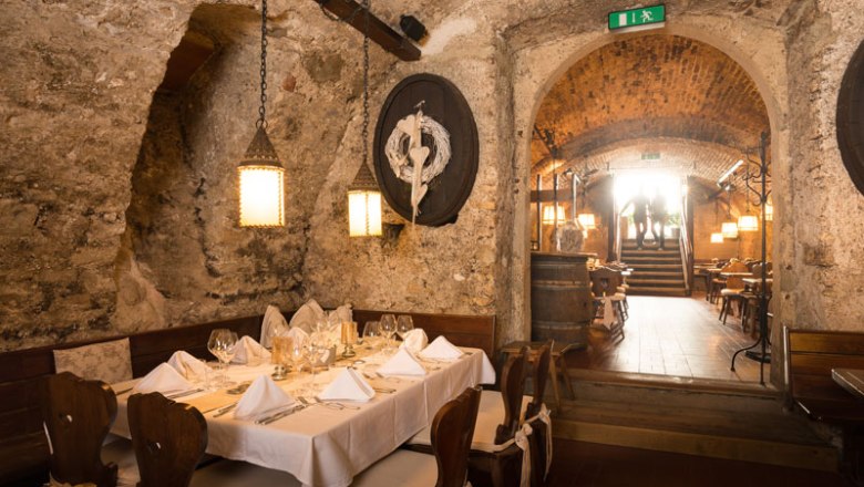 Cellar Old Zechhaus, © Wastian A rustic cellar restaurant with a laid table, stone walls and wooden furniture.