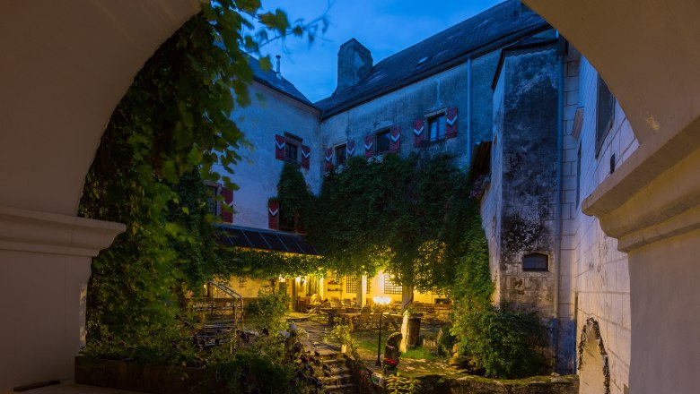 Plankenstein Castle, © zVg Inner courtyard of Plankenstein Castle at dusk, illuminated with warm light, surrounded by ivy and old walls.