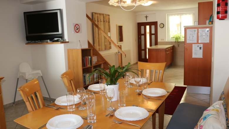 Dining area Kitchen Entrance Guests 6, © Gruber Claudia Dining area with set table, TV, bookshelf and kitchen in the background.